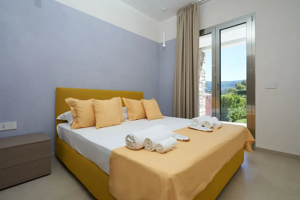 Camera da letto con biancheria gialla e porta finestra sul giardino